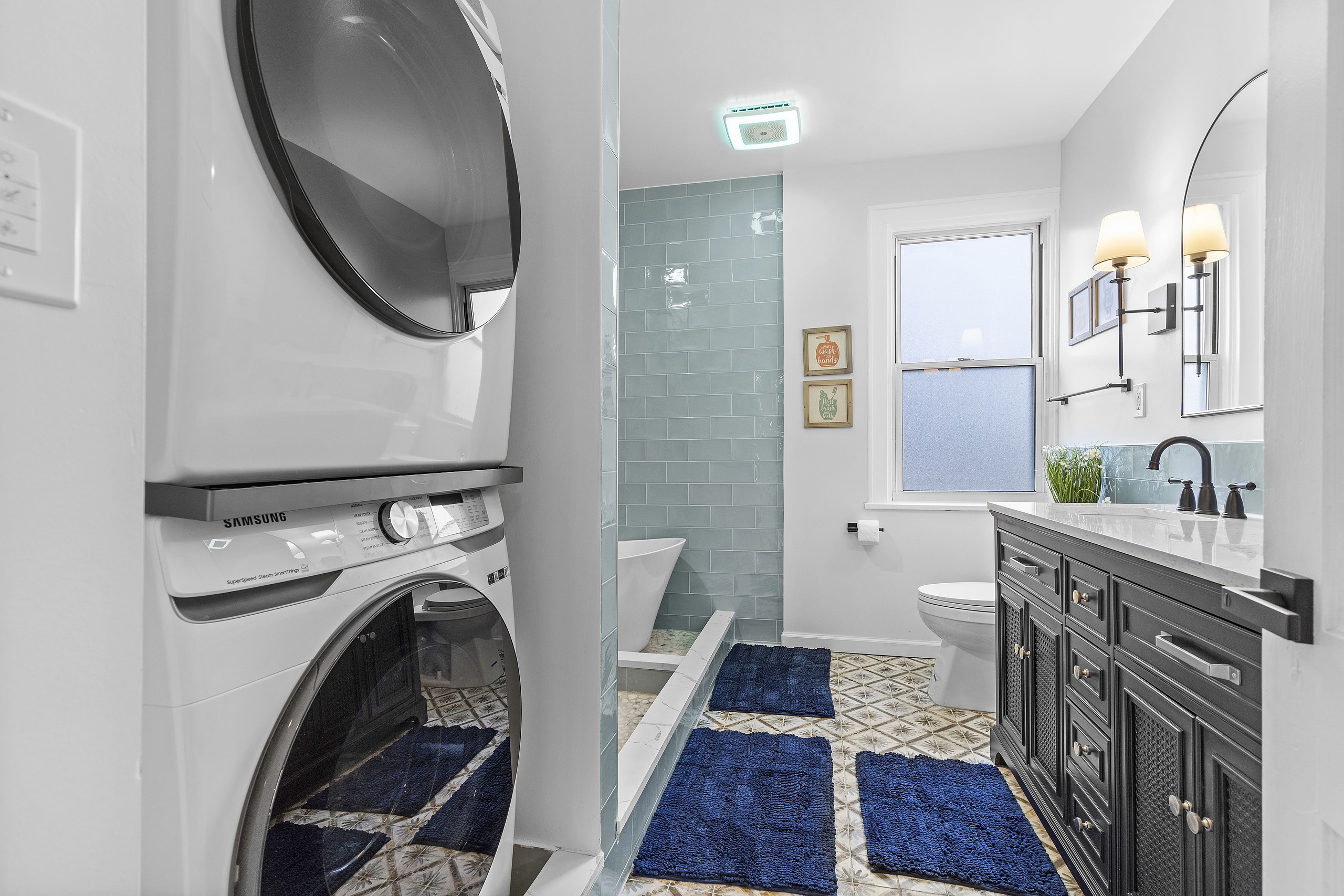 After renovation, a modern and stylish vacation rental bathroom with a blue tile shower and sleek dark vanity.