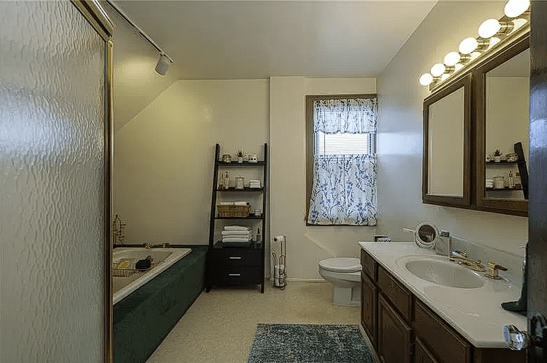 Before renovation, a dated vacation rental bathroom with a green tub and wooden cabinets.