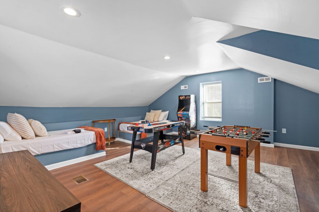 A vibrant vacation rental interior design featuring a foosball table, arcade game, and cozy sitting area with plush pillows.
