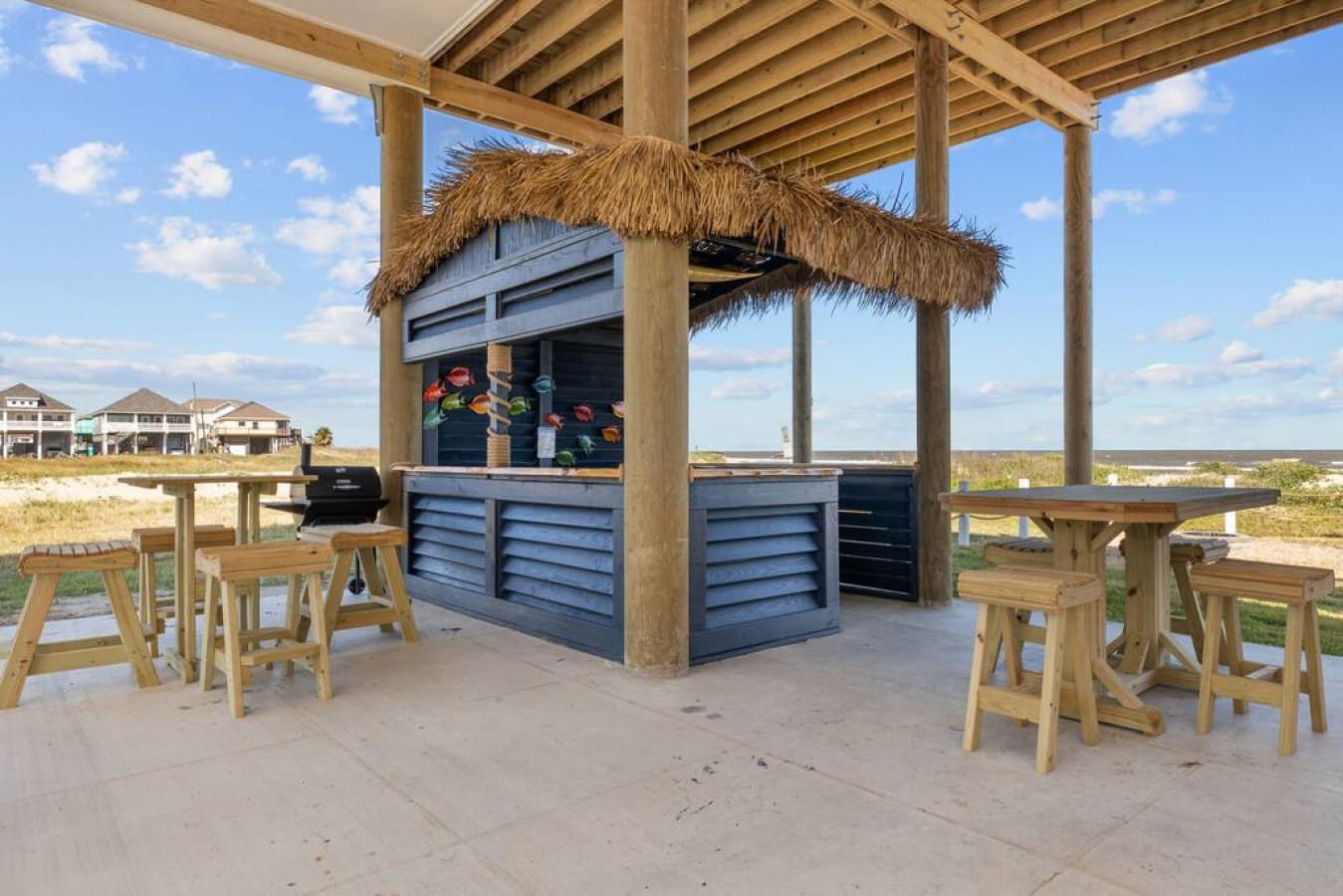 Beachside outdoor bar area in a vacation rental designed by Kindred Design, featuring a thatched roof and bar stools.