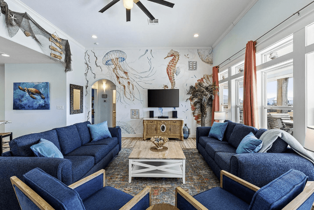 Coastal-themed vacation rental living room designed by Kindred Design with plush blue sofas and ocean-inspired wall art.